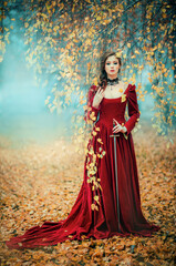 Portrait of magnificent Fashion gothic girl standing in autumn forest .Fantasy art work.Amazing red haired model in claret dress with a sword .Fairytale about young princess-warrior. 