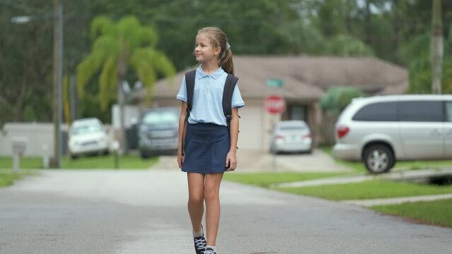 Young student girl walking on suburban street returning home from school