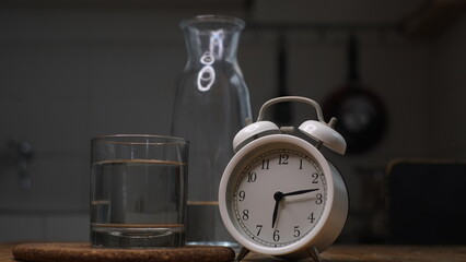 Alarm clock, a glass and a bottle of water on dark background, conceptual photo, reminder to drink...
