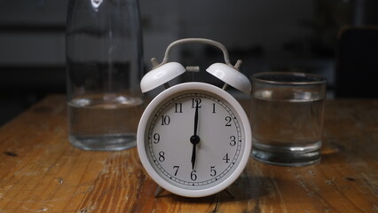 Alarm clock, a glass and a bottle of water on dark background, conceptual photo, reminder to drink water to replace body fluids