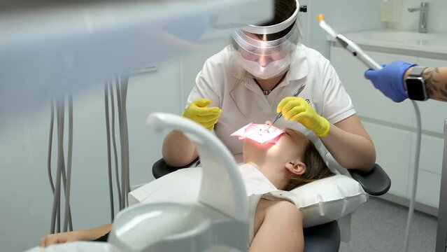 dentistry adolescence a doctor in yellow gloves fills a tooth of a young girl for a woman close-up video in dentistry at the dentist drying the tooth with light new technologies. modern clinic