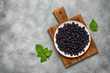 Black raspberries in a plate on a wooden board, gray stone background. Top view, flat lay.