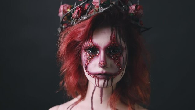 Young red hair woman with haloween bloody face art, horror mystery look isolated on black background