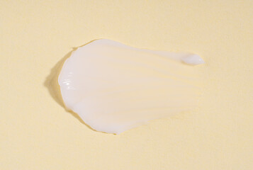 Texture of the white cream on a yellow background. White cream smudge swatch textured. Cosmetic smear of creamy texture on a pastel yellow background