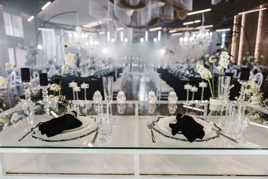 Wedding set up, dinner table reception. Serving, setting newlyweds table. Plate and glass, stack, wineglass, luxury rich decor, black napkin. Birthday, event. Restaurant interior. Side view.