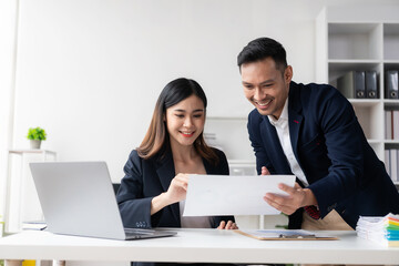 Two Asian business men and women smiling happily working with laptops and financial documents. They...
