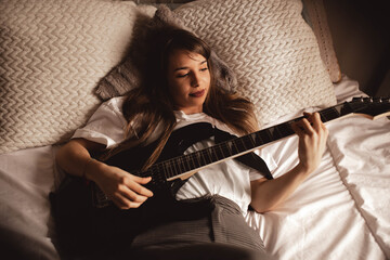 Young brunette woman playing guitar on bed