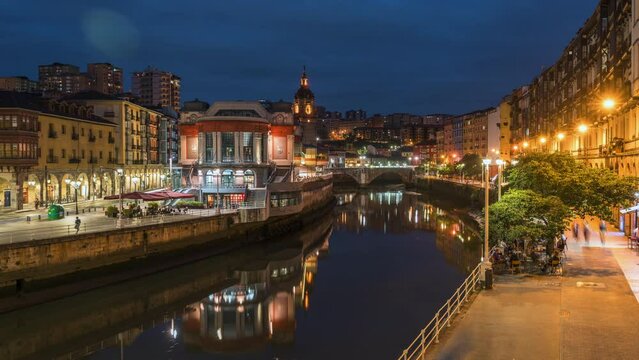 Dusk to night timelapse view of Bilbao cityscape including the historic La Ribera food market in Bilbao, Basque Country, Spain, zoom out. 