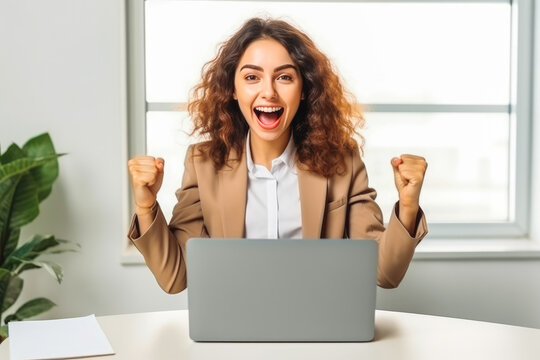 Excited young woman sitting at table with laptop and celebrating.