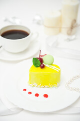 A cup of coffee with a heart-shaped cake in yellow glaze on a plate on a light background