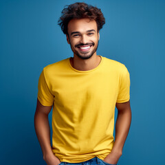 Fototapeta na wymiar portrait of a young man smiling. direct eye contact. yellow t-shirt, unclutterd plain blue background