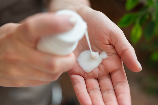 Close up woman hand pressing white plastic pump container and another hand taking white cream on it. Beauty procedure, professional and home cosmetology, health care concepts