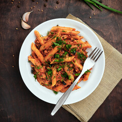 Traditional Italian cuisine: tasty pasta with bolognese sauce. Yummy macaroni (penne rigate) on rough wooden table. Top view. Square