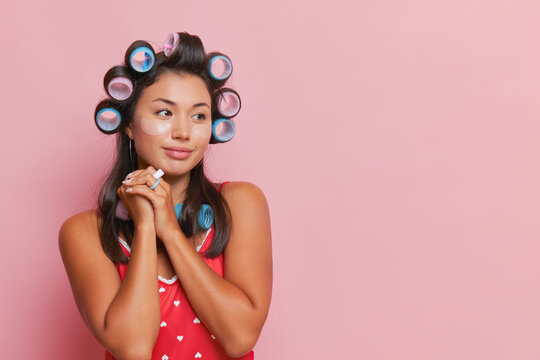 Close-up brunette girl with hair curlers pressing her hands to her chest while posing on pink backdrop, good mood concept, copy space