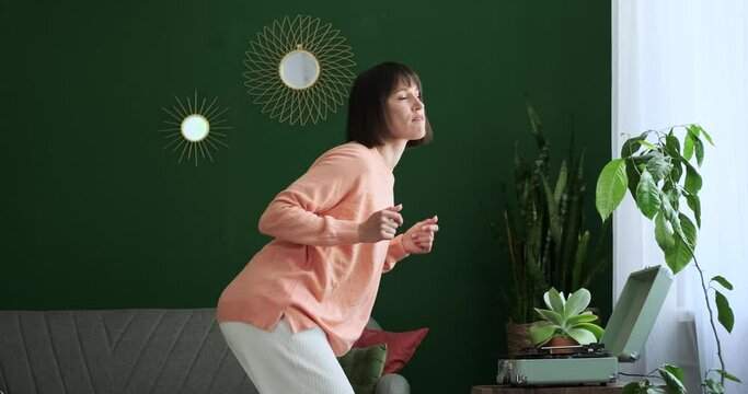In the inviting living room, a Caucasian woman skillfully starts a vinyl record player and then lets the music guide her into a dance. Her graceful movements and joyful expression create.