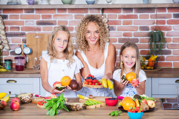 Mother and daughters cooking together in the kitchen. Healthy food concept. Portrait of happy family with fresh smoothies. Happy sisters.