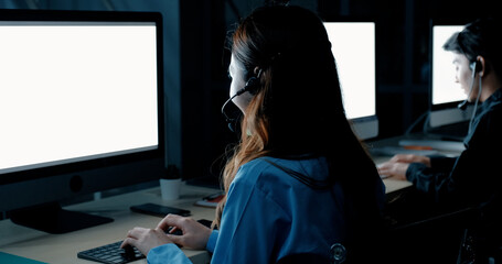 Businesswoman in headset using laptop. Side view of young serious call center operator working with laptop computer in dark office. Client service concept