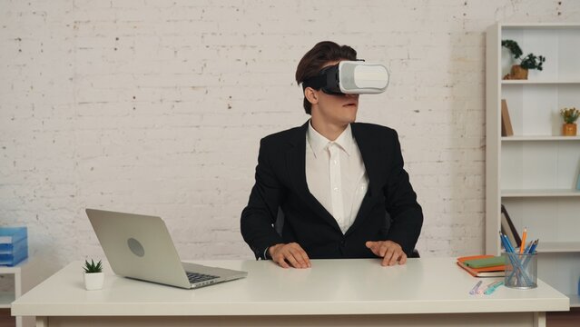 Medium shot of a young man in an office wearing virtual reality, vr helmet, gear, looking at, interacting with an invisible screen excited and happy.