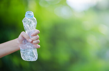 Hand squeezing a plastic bottle on a green background. It represents the movement against pollution...