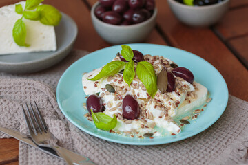 Feta cheese sliced on blue plate with sesame, flax seeds, served with black olives and basil leaves. Delicious and healthy breakfast on terrace
