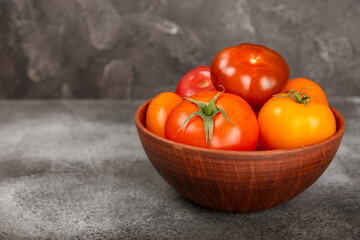 Tomatoes on marble texture background. Cherry tomatoes, yellow, pink, brown and black tomatoes in a bowl. Organic vegetables, harvesting.Vegan. Fresh ripe tomatoes. copy space.