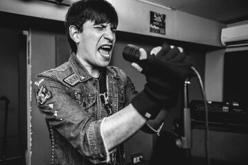 Passionate and intense young rocker vocalist unleashing raw energy during intense metal performance in a rehearsal room (in black and white)