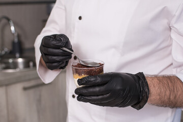 Close-up of a male pastry chef decorating a dessert in the kitchen, a male chef preparing a trifle in a glass cup