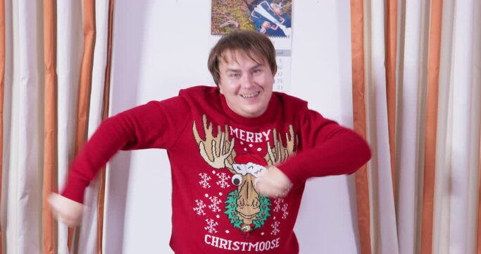 Silly-looking man in Christmas knitted ugly sweater with deer funny dances absurd dance waves arms rejoices. Merry new year family party musical greetings, finger dance. Crazy New Year fun of guests