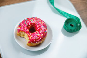 bitten sweet donut and a measuring tape. Unhealthy eating and obesity concept