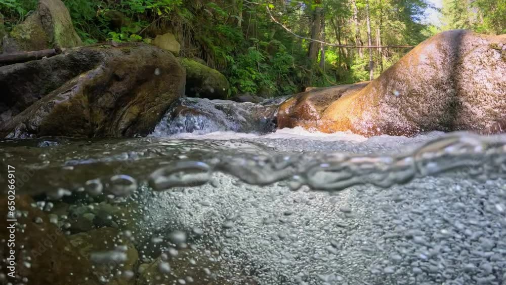 Poster half underwater slow motion shot of stream between stones with small waterfalls. river with clear wa