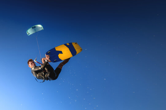 A kitesurfer rides while suspended in the air. Kitesurfer jumps against a beautiful blue sky background catching his board in the air
