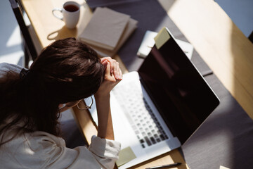Overhead shot of exhausted freelancer sitting near laptop and books on table at home