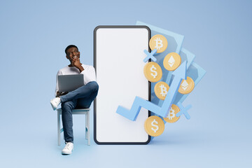 Cheerful black man trader using laptop, sitting by huge phone