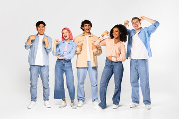 Group of happy teen multiracial friends standing over white background, pointing at themselves and...