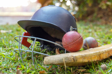 Cricket equipment is a cricket ball, cricket bat, cricket helmet on a grass background. Soft and...