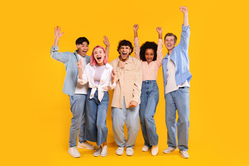 Fototapeta premium Winner concept. Group of diverse teen friends clenching fists, standing together over yellow background