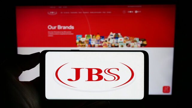 Stuttgart, Germany - 09-17-2023: Person holding smartphone with logo of Brazilian mear processing company JBS S.A. on screen in front of website. Focus on phone display.