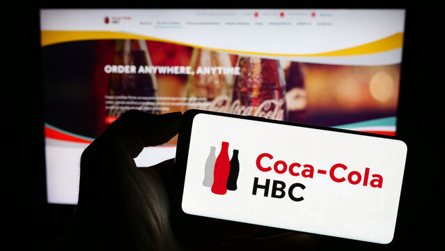 Stuttgart, Germany - 09-18-2023: Person holding cellphone with logo of beverage company Coca-Cola HBC AG on screen in front of business webpage. Focus on phone display.