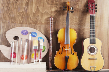 Attributes of the arts. Painting, music. Art palette, brushes, violin on a wooden textured...