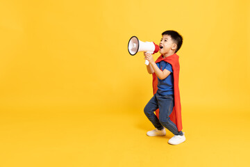 Superhero Asian boy with red cape holding megaphone isolated on yellow background, Wow and Announce...