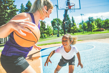 Mother and little daughter play basketball outside