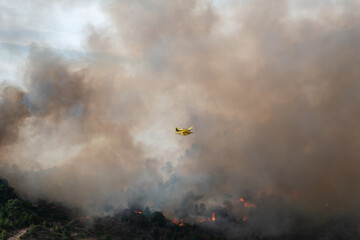 Avião bombeiro a sobrevoar um incêndio florestal devastador que deixa muito fumo no ar