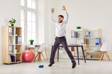 Happy funny fit smiling young business man or corporate employee doing star jumps during a quick...