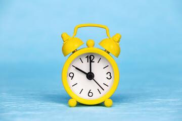 Yellow retro alarm clock on blue background. Daylight savings time.