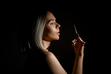 Obraz premium Beautiful blonde hairdresser woman holding scissors against face over black background , studio shot