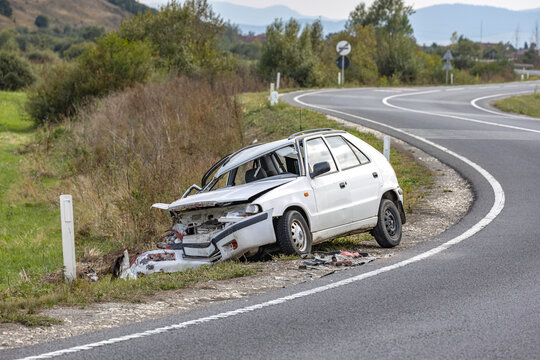 White car wrecked on the side of the road, abandoned after a head-on collision accident