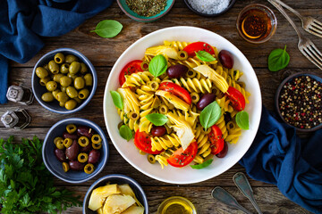 Antipasto pasta salad - fusilli pasta with various vegetables on wooden background