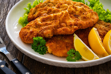 Crispy breaded seared chicken cutlet with lemon slices and fresh vegetables on wooden table
