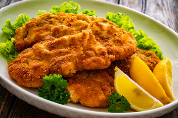 Crispy breaded seared chicken cutlet with lemon slices and fresh vegetables on wooden table
 - obrazy, fototapety, plakaty