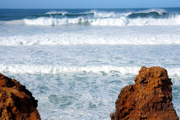 big waves rolling and breaking against cliff with high fountain of splashing water                              